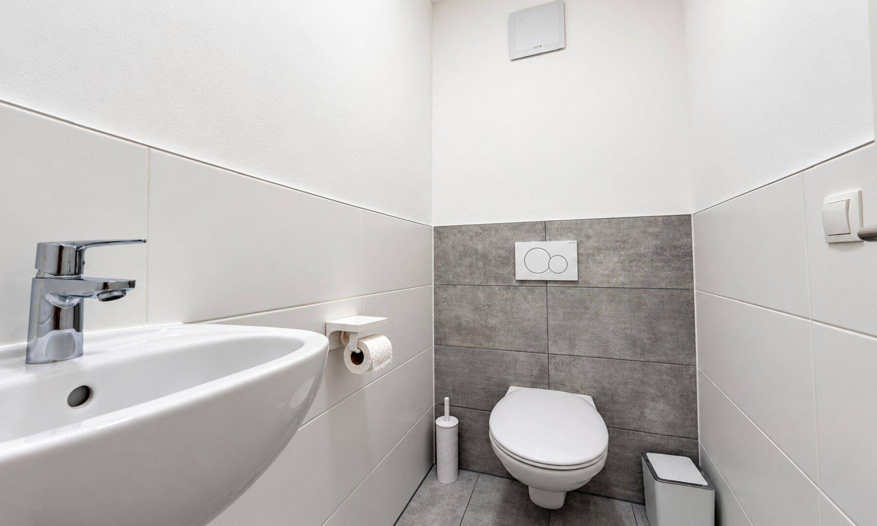 Modernes Gäste-WC mit Wand-WC, Waschbecken und stilvollen grauen Fliesen.