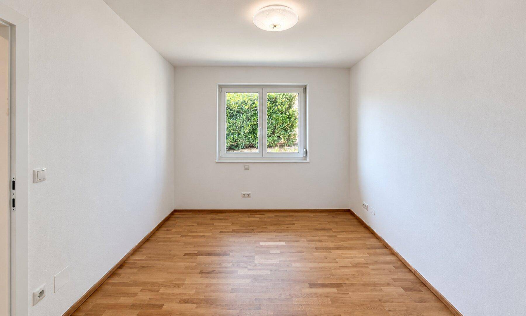 Helles Zimmer mit Holzboden und Fenster, vielseitig nutzbar als Schlaf- oder Arbeitszimmer.