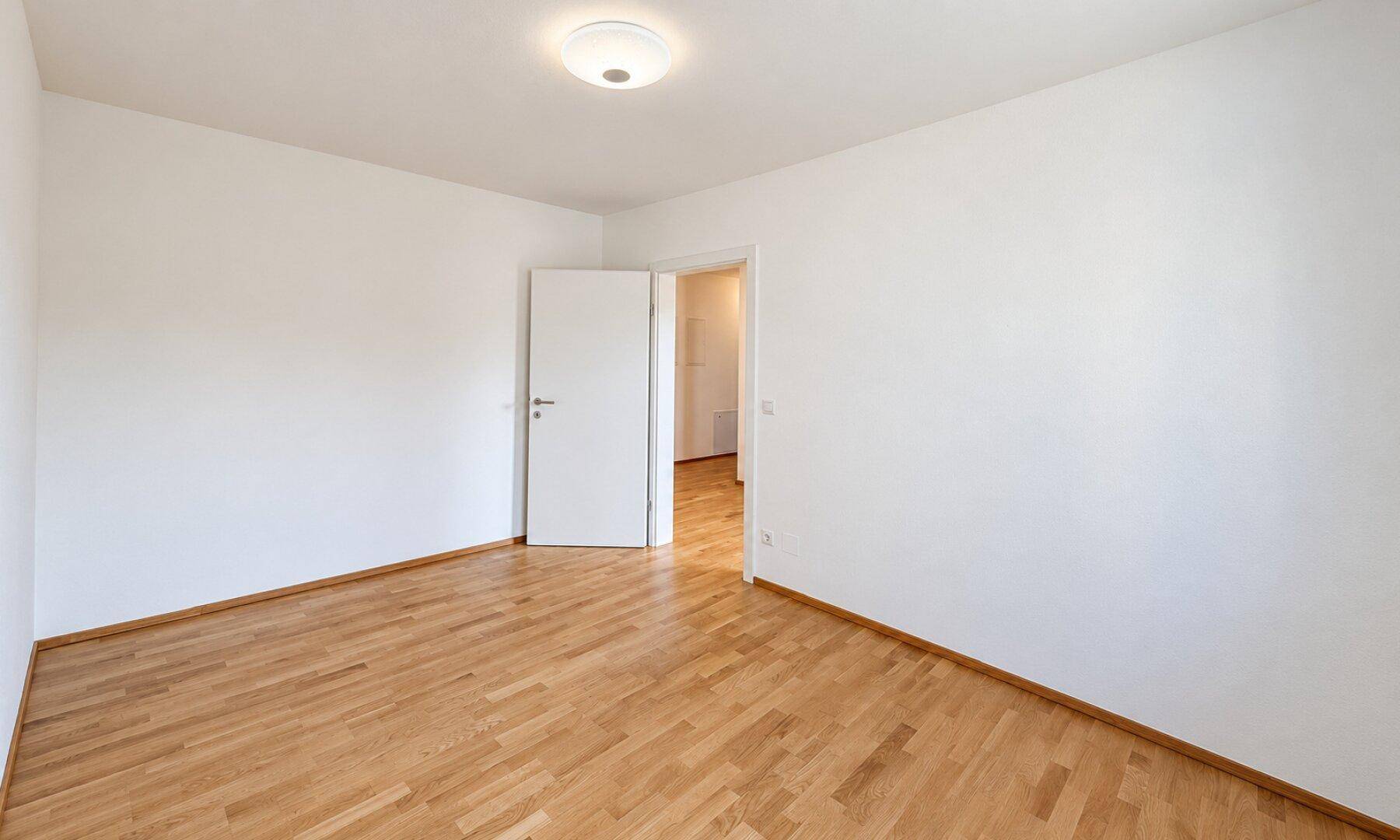 Leeres Zimmer mit Holzboden und weißer Tür, bietet eine neutrale Basis für Einrichtung.