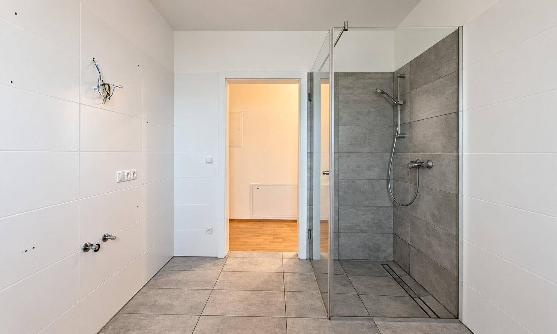 Modernes Badezimmer mit ebenerdiger Dusche, grauen Bodenfliesen und weißen Wandfliesen.