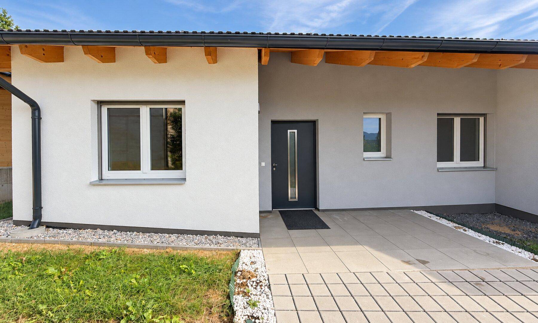 Eingangsbereich des modernen Hauses mit dunkler Haustür und gepflastertem Zugang.
