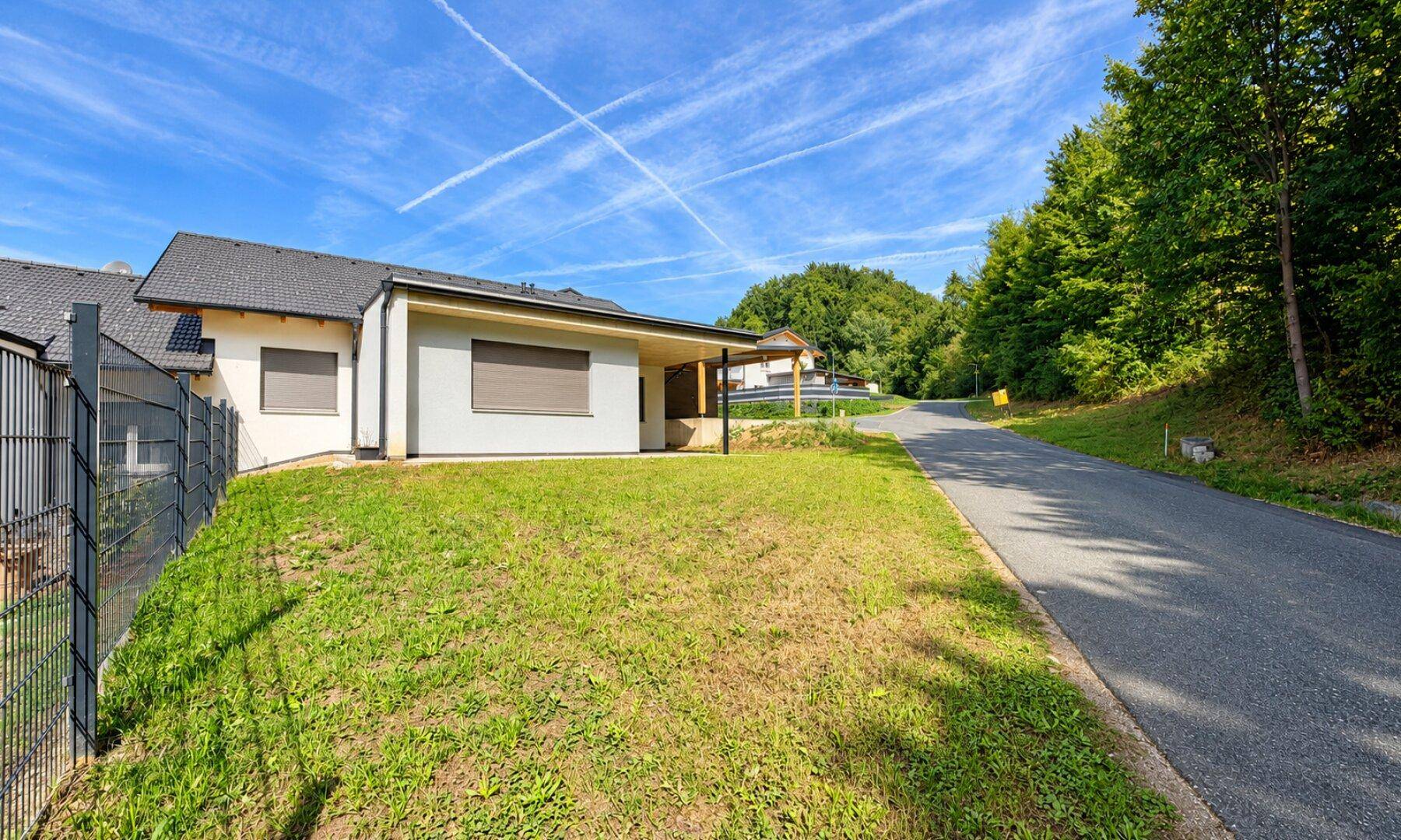 Seitenansicht des Hauses mit Rasenfläche, Zaun und angrenzender Straße.