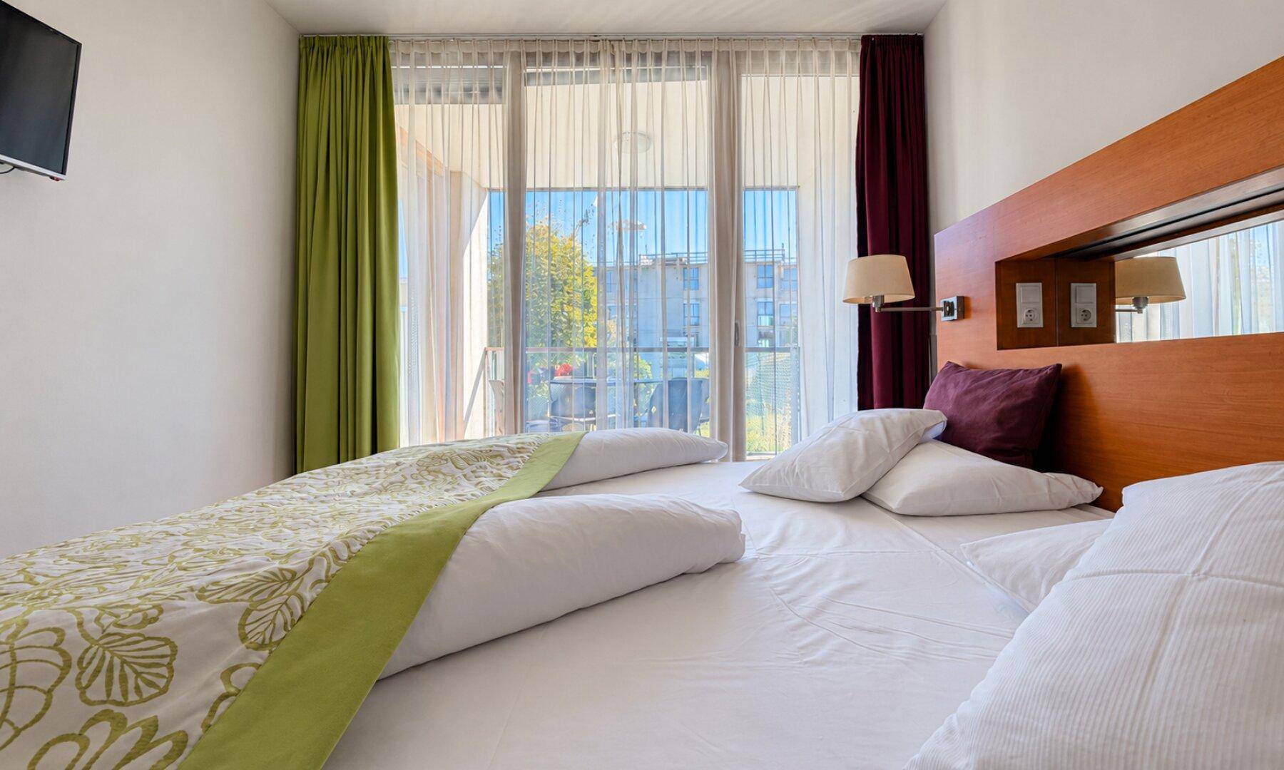 Schlafzimmer mit Doppelbett, Holzkopfteil und Zugang zu einem Balkon durch große Fenster.