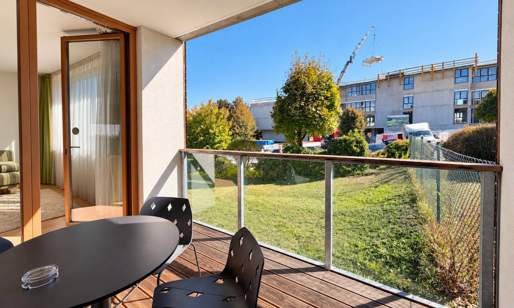 Sonniger Balkon mit Holzboden, Tisch und Stühlen, bietet Blick auf die Umgebung.