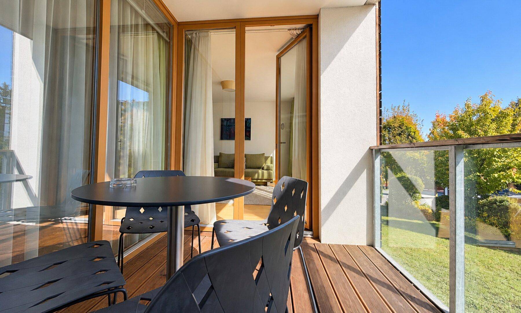 Balkon mit Holzboden, Sitzgelegenheiten und Blick auf den Garten und die Umgebung.