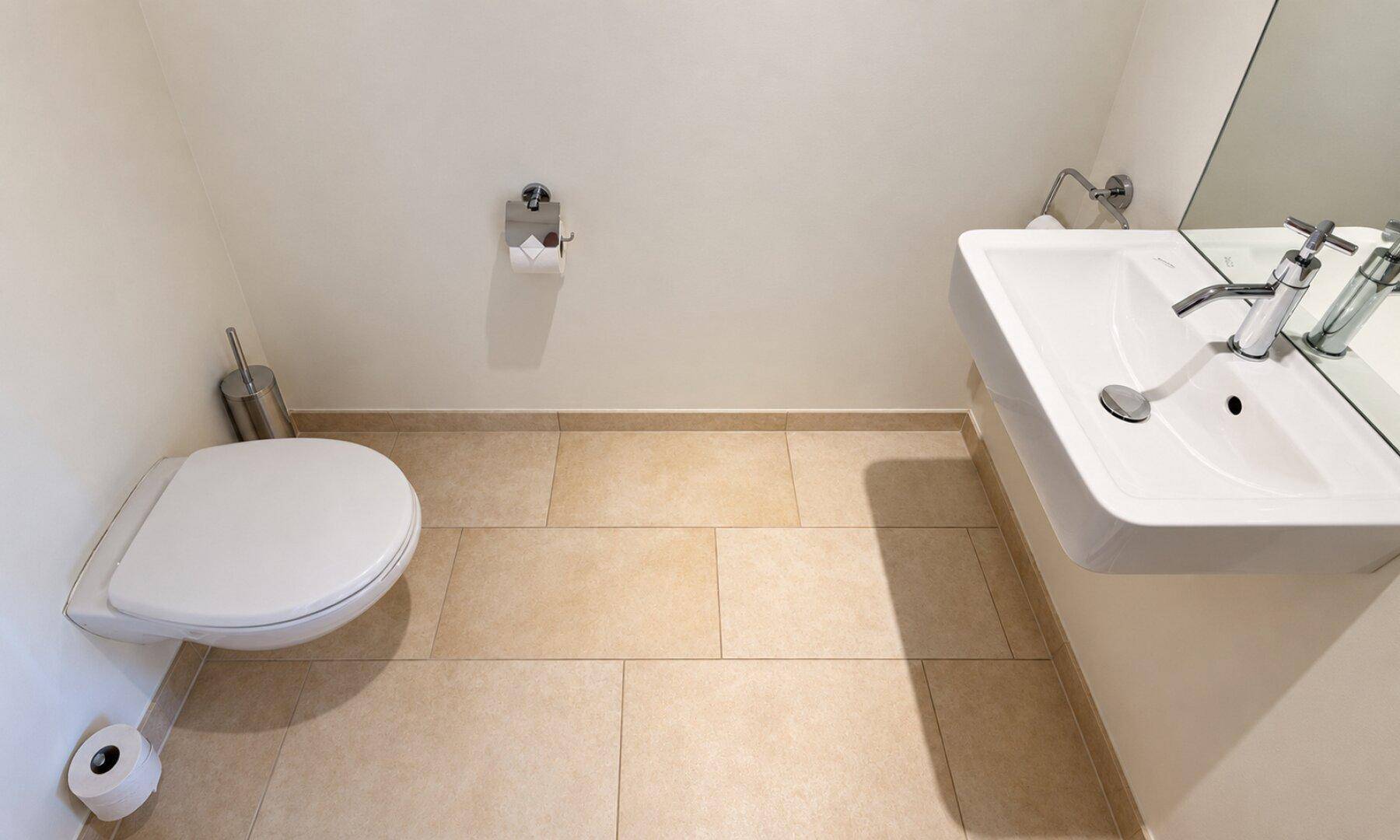 Kleines Gäste-WC mit wandhängendem WC, Waschbecken und hellen Fliesen.