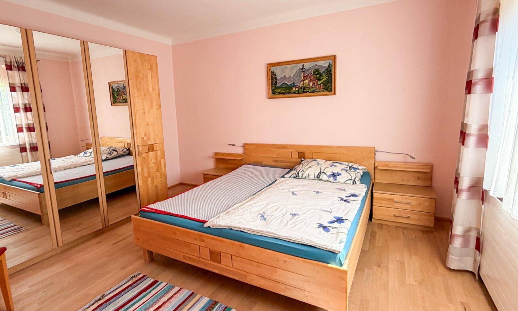 Schlafzimmer mit rosa Wänden, Doppelbett aus hellem Holz und Spiegelschränken.