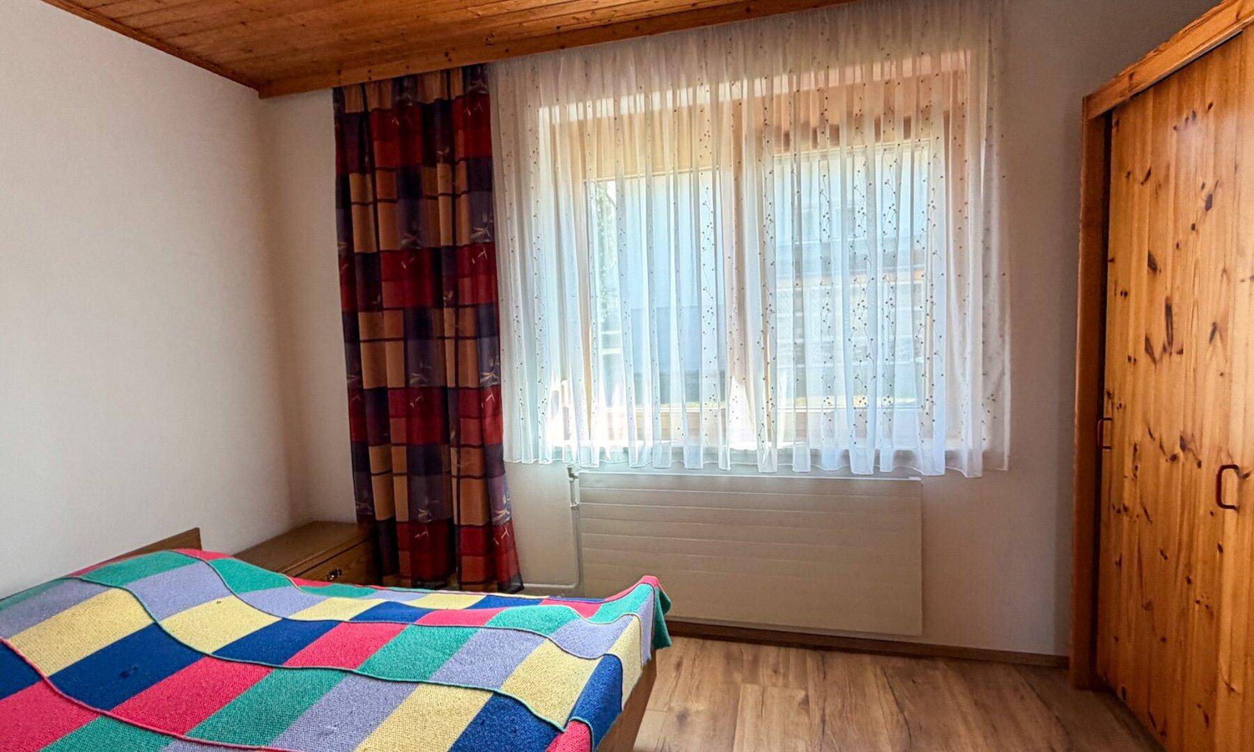 Schlafzimmer mit Holzbalkendecke, Einzelbett und bunten Vorhängen.