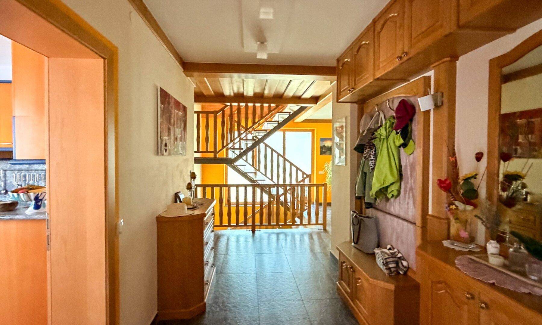 Geräumiger Flur mit Holztreppe, Fliesenboden und Garderobe in warmen Farbtönen.