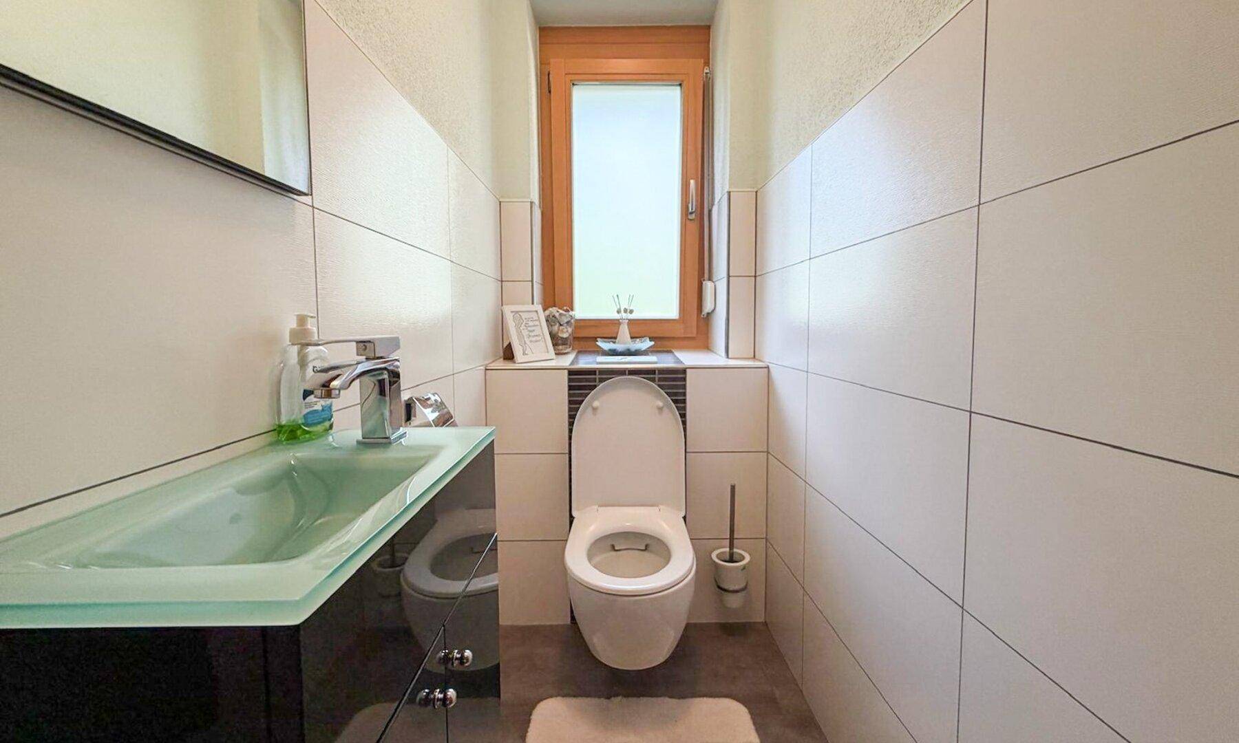 Modernes Gäste-WC mit weißen Fliesen, Fenster und grünem Waschbecken.