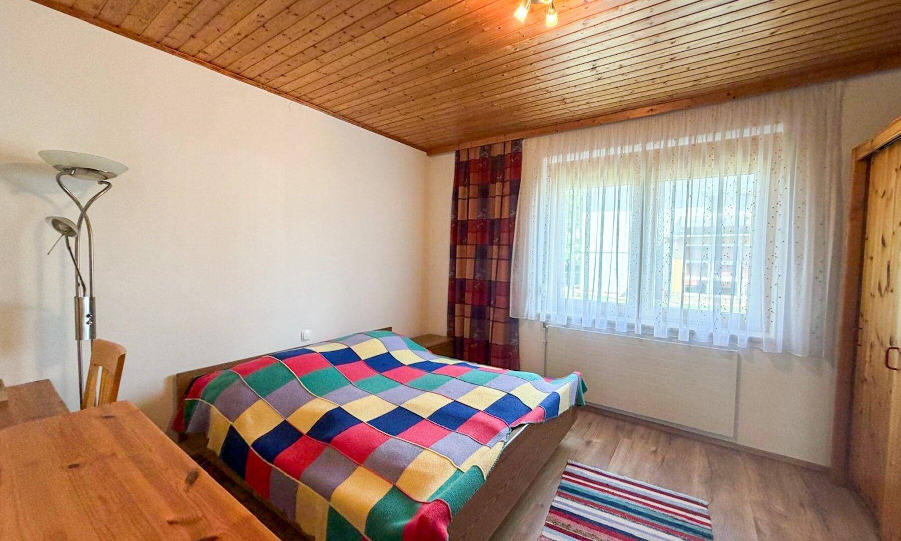 Gemütliches Schlafzimmer mit Holzbalkendecke, Einzelbett und bunten Vorhängen.