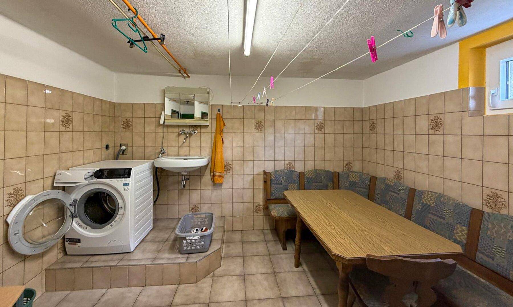 Kellerraum mit Waschmaschine, gefliesten Wänden und einer traditionellen Eckbank mit Tisch.