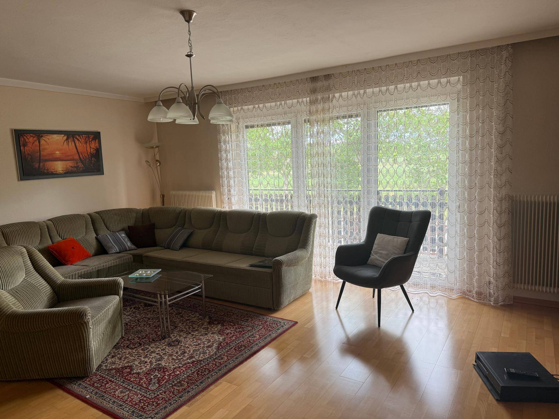 Gemütliches Wohnzimmer mit Ecksofa, Parkettboden und großem Fenster für viel Tageslicht.