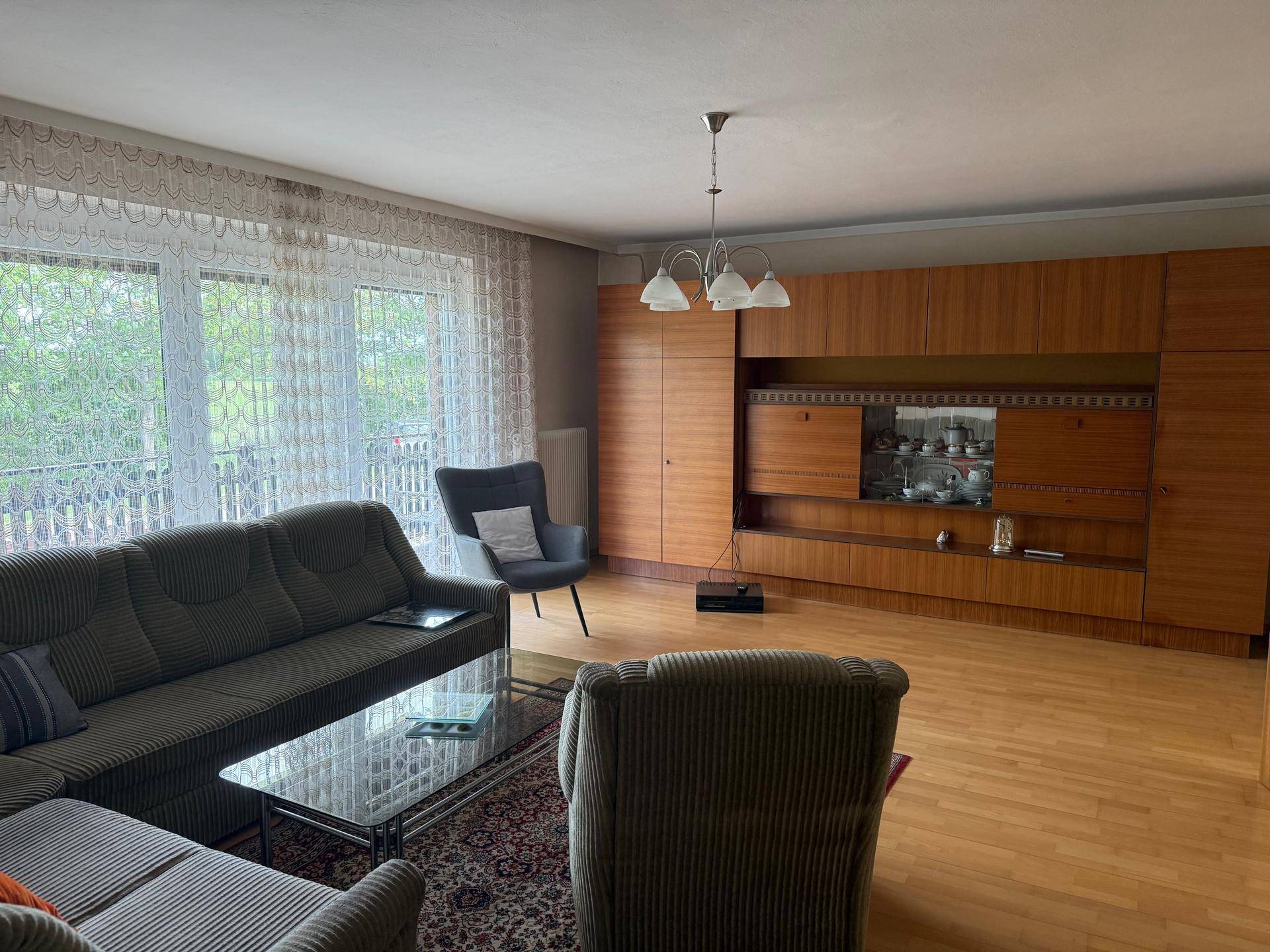 Helles Wohnzimmer mit klassischer Holzschrankwand und Parkettboden, ideal für Familien.