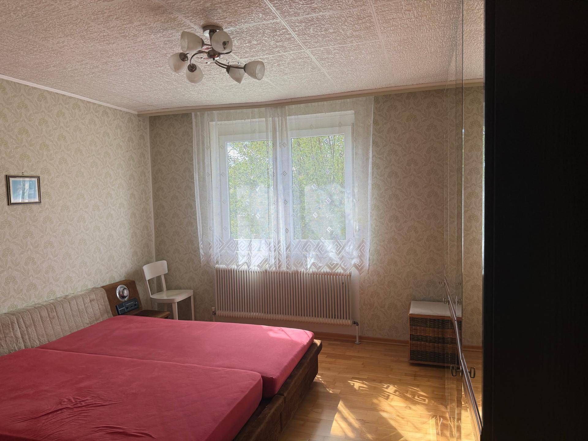 Schlafzimmer mit zwei Einzelbetten, Parkettboden und Fenster für angenehmes Tageslicht.
