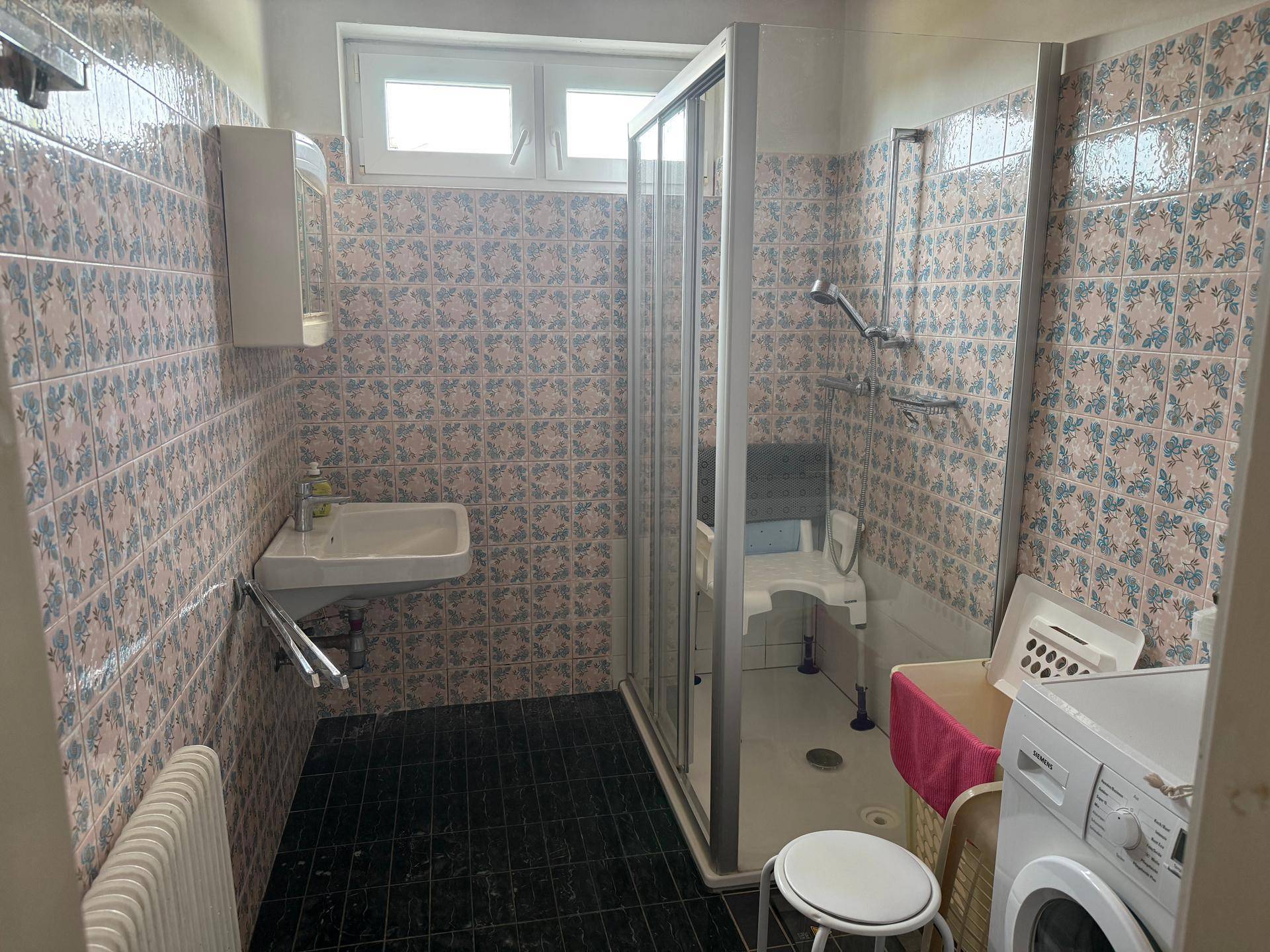 Badezimmer mit Duschkabine, Waschbecken und Waschmaschine, ausgestattet mit bunten Fliesen.