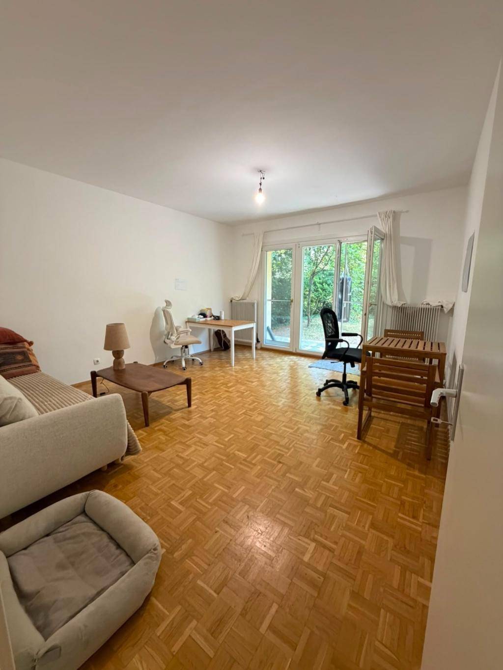 Geräumiges Wohnzimmer mit Parkettboden, Arbeitsbereich und Zugang zu einem Außenbereich.