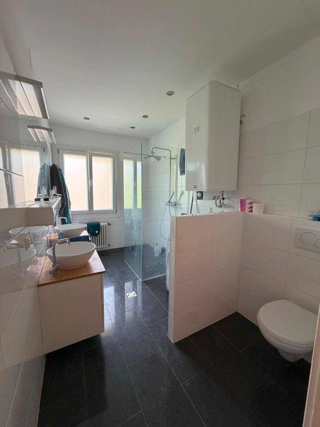 Modernes Badezimmer mit Doppelwaschbecken, begehbarer Dusche und dunklen Fliesen.