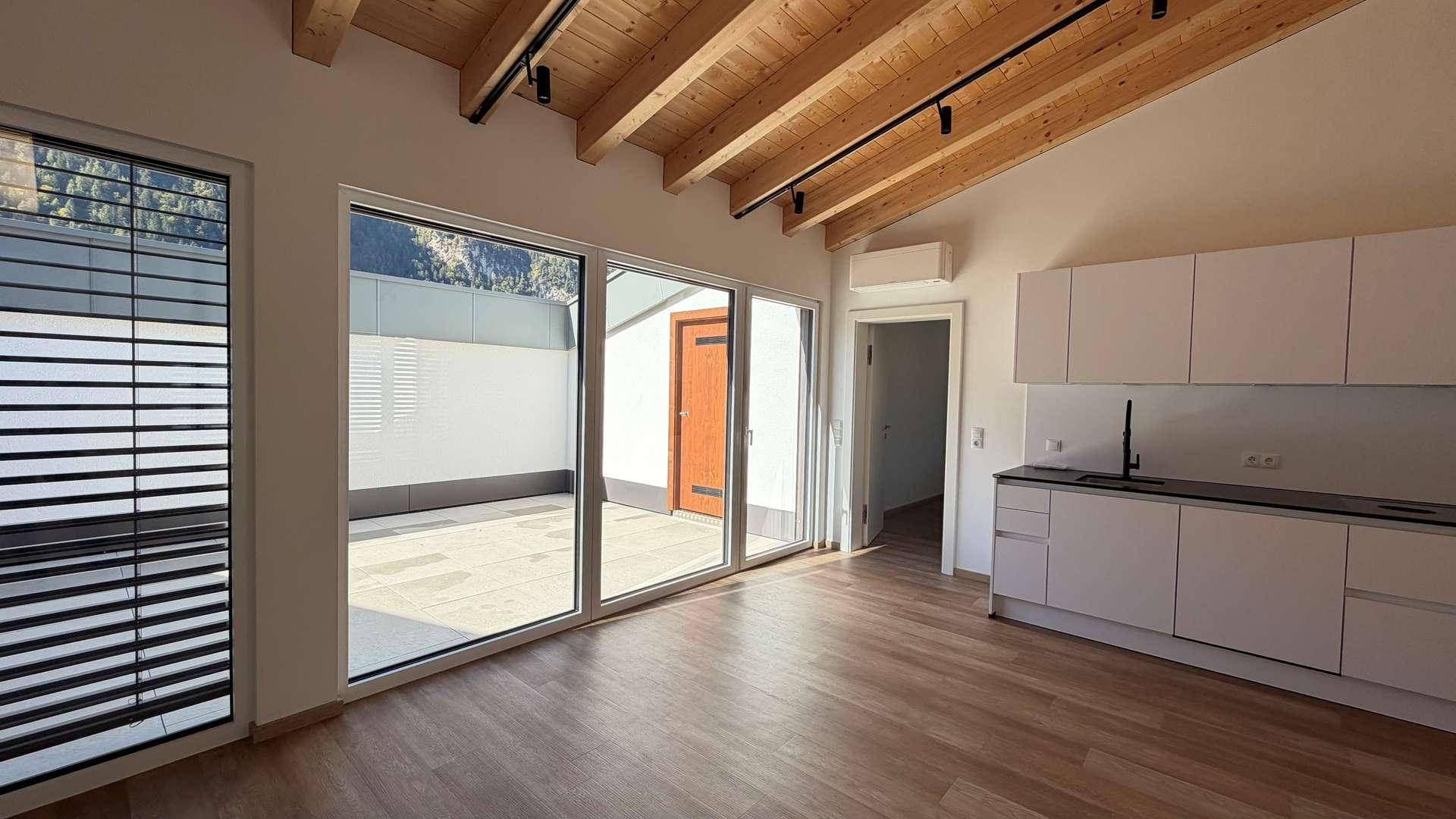 Lichtdurchfluteter Wohnbereich mit offener Küche, Holzbalken und Zugang zur Sonnenterrasse.