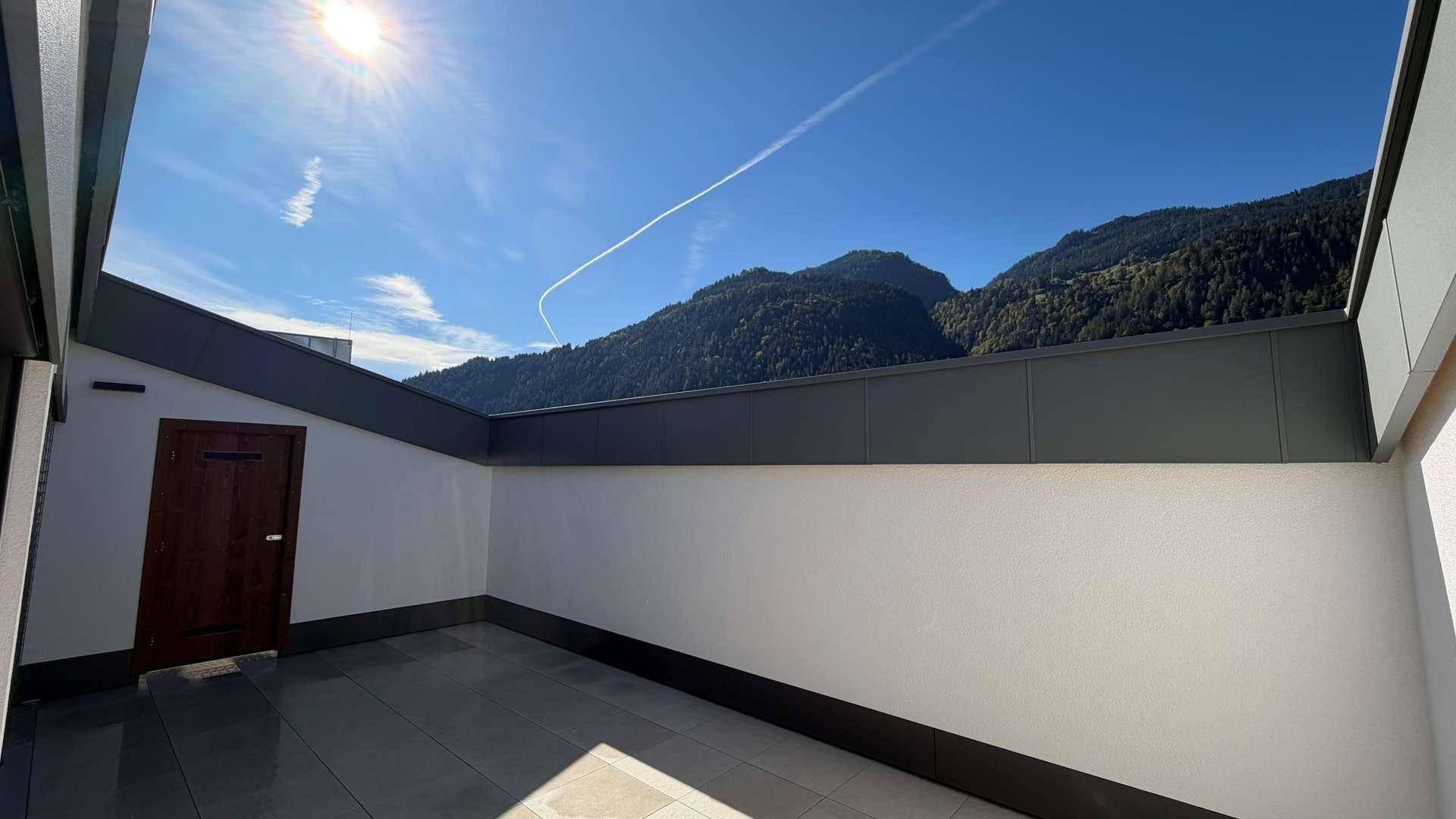 Helle Terrasse mit Fliesenboden und beeindruckendem Panoramablick auf die Berge.