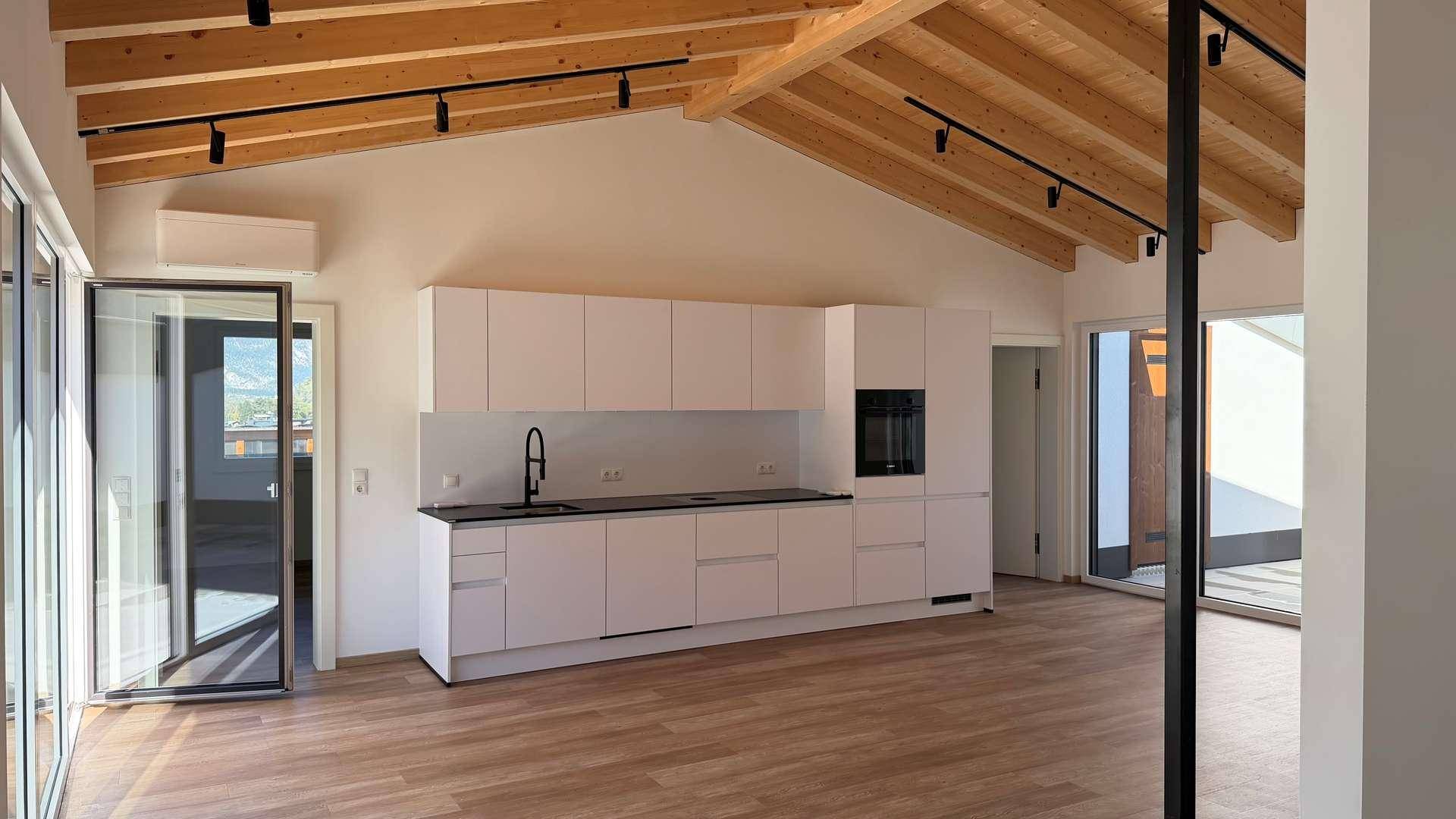 Moderne Küche in offenem Wohnbereich mit Holzbalkendecke und Zugang zu Außenbereichen.
