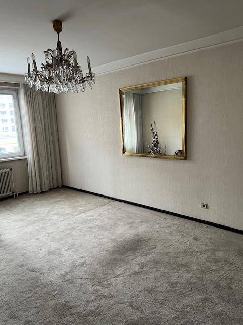 Leeres Zimmer mit Teppichboden, einem Kronleuchter und einem großen Wandspiegel.