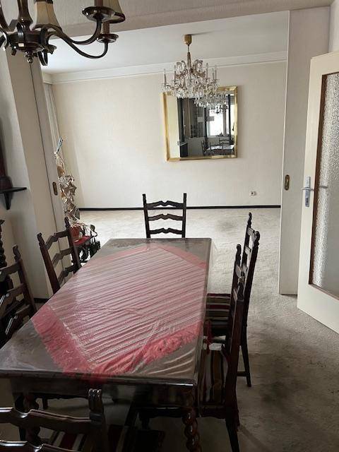 Esszimmer mit Holztisch und Stühlen, Teppichboden und einem Kronleuchter im Hintergrund.