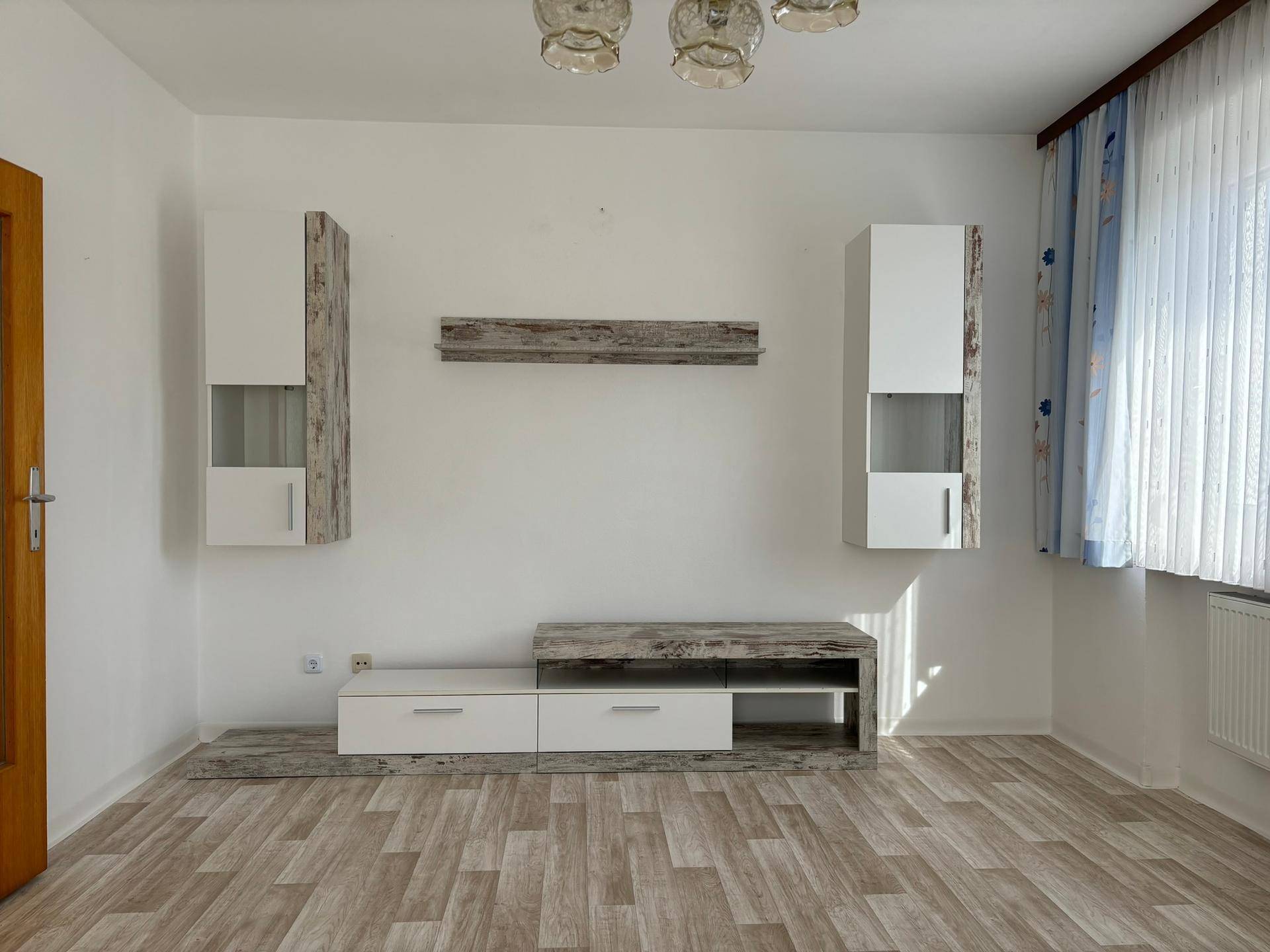 Leeres Wohnzimmer mit modernem Laminatboden und Wandregalen, bereit zur individuellen Gestaltung.