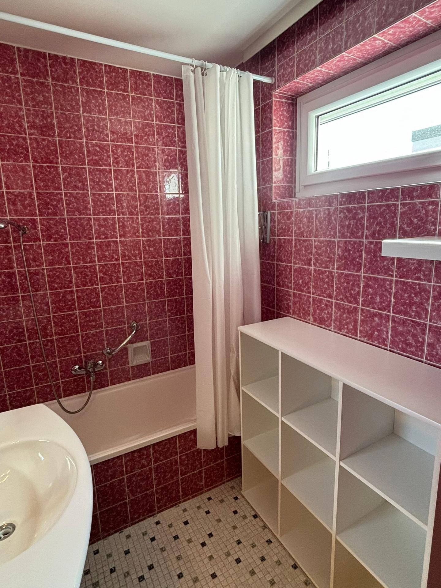 Badezimmer mit roten Fliesen, Badewanne und Fenster, das für natürliche Belüftung sorgt.