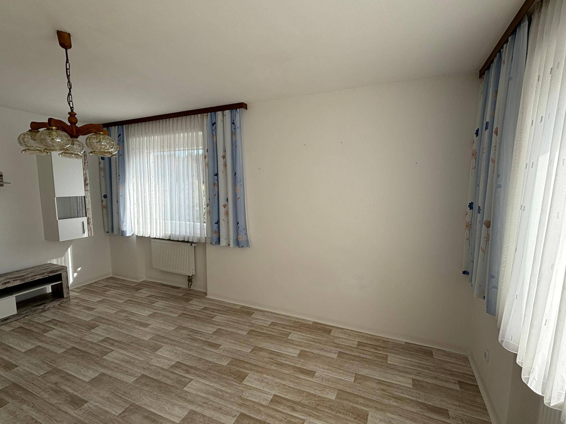 Helles Wohnzimmer mit Laminatboden und zwei Fenstern, die viel Tageslicht hereinlassen.
