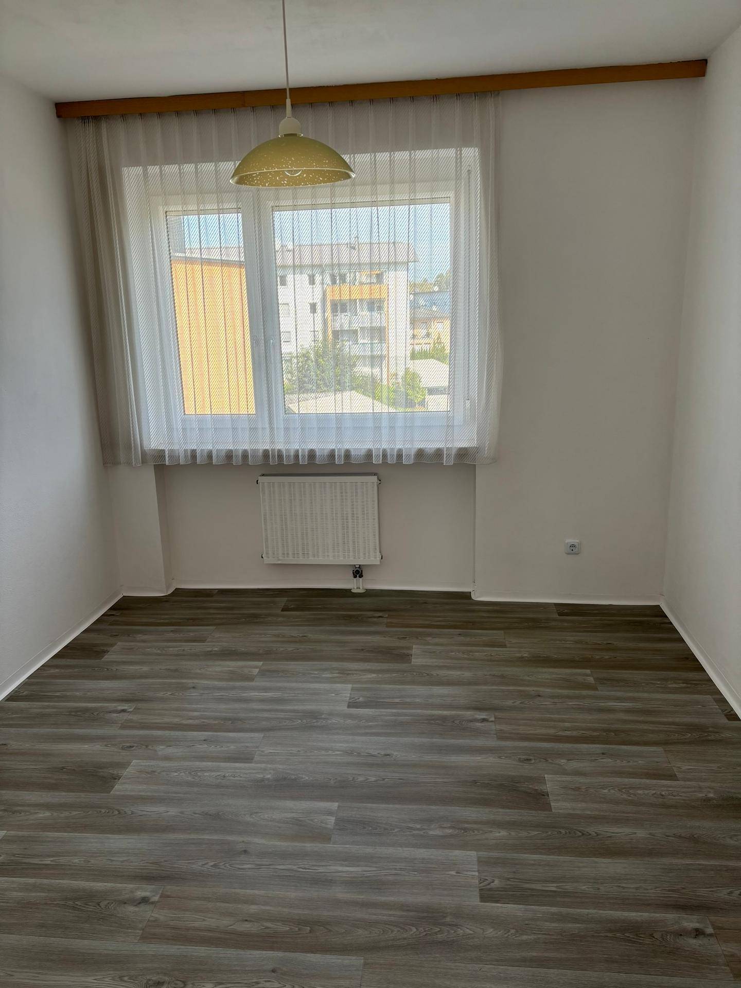 Heller Raum mit modernem Laminatboden und großem Fenster, das viel Tageslicht hereinlässt.