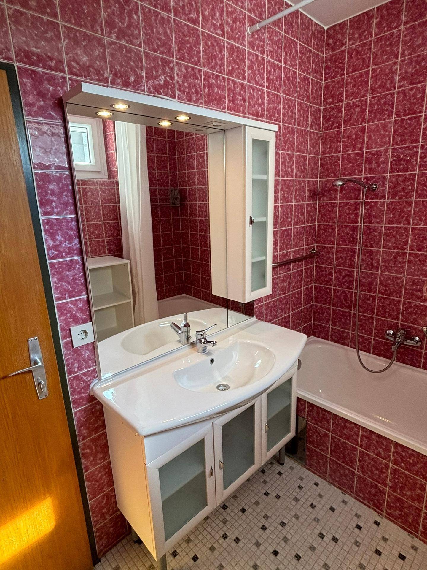 Badezimmer mit roten Fliesen, Badewanne und Waschbeckenunterschrank, in gutem Zustand.