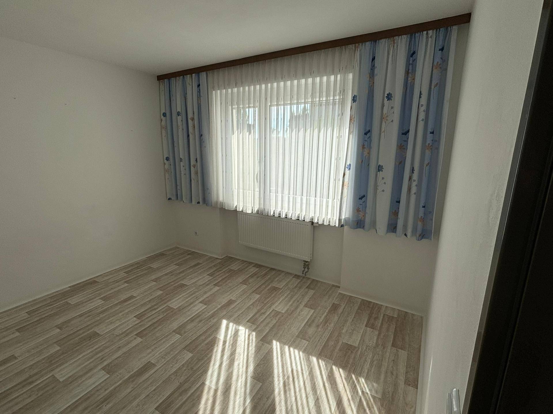 Sonniger Raum mit Laminatboden und großem Fenster, das viel natürliches Licht bietet.