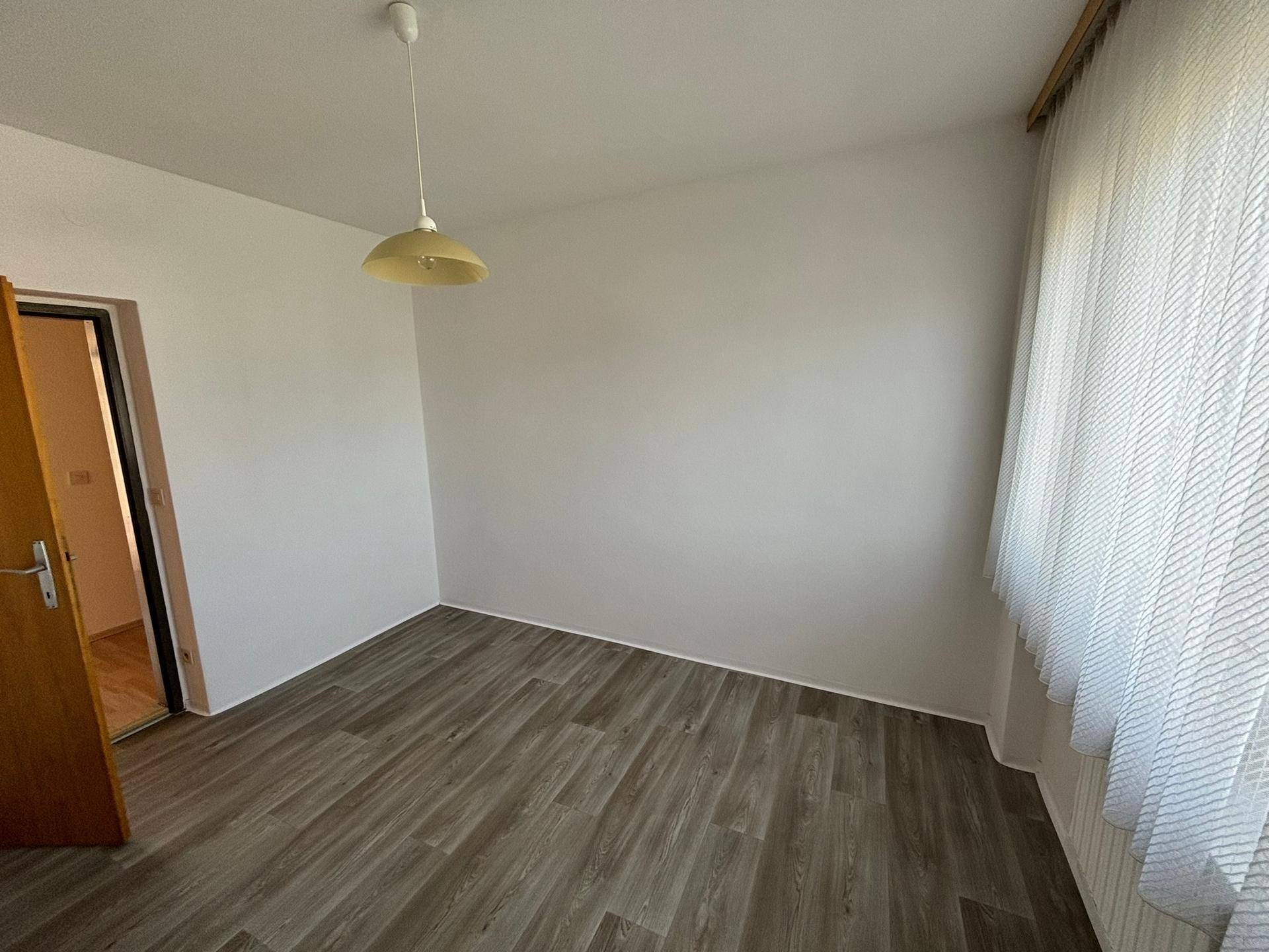 Leerer Raum mit Laminatboden und großem Fenster, ideal als Schlaf- oder Arbeitszimmer.