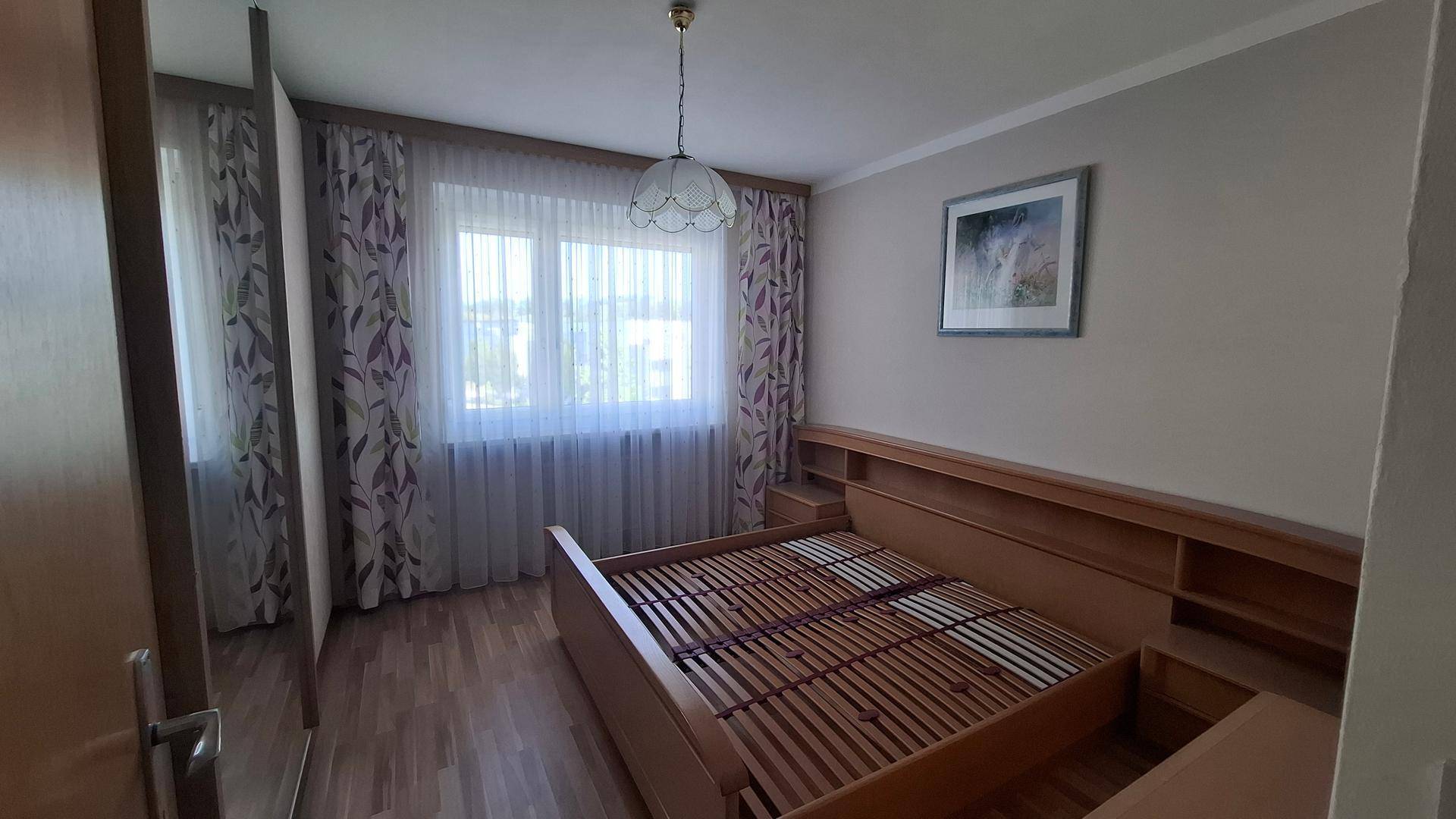 Schlafzimmer mit Holzbettrahmen, Einbauschränken und Fenster mit Blick nach draußen.