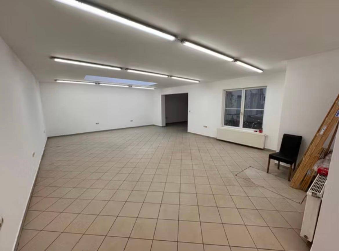 Großer, heller Raum mit Fliesenboden, weißen Wänden und einer Deckenluke für zusätzliches Licht.