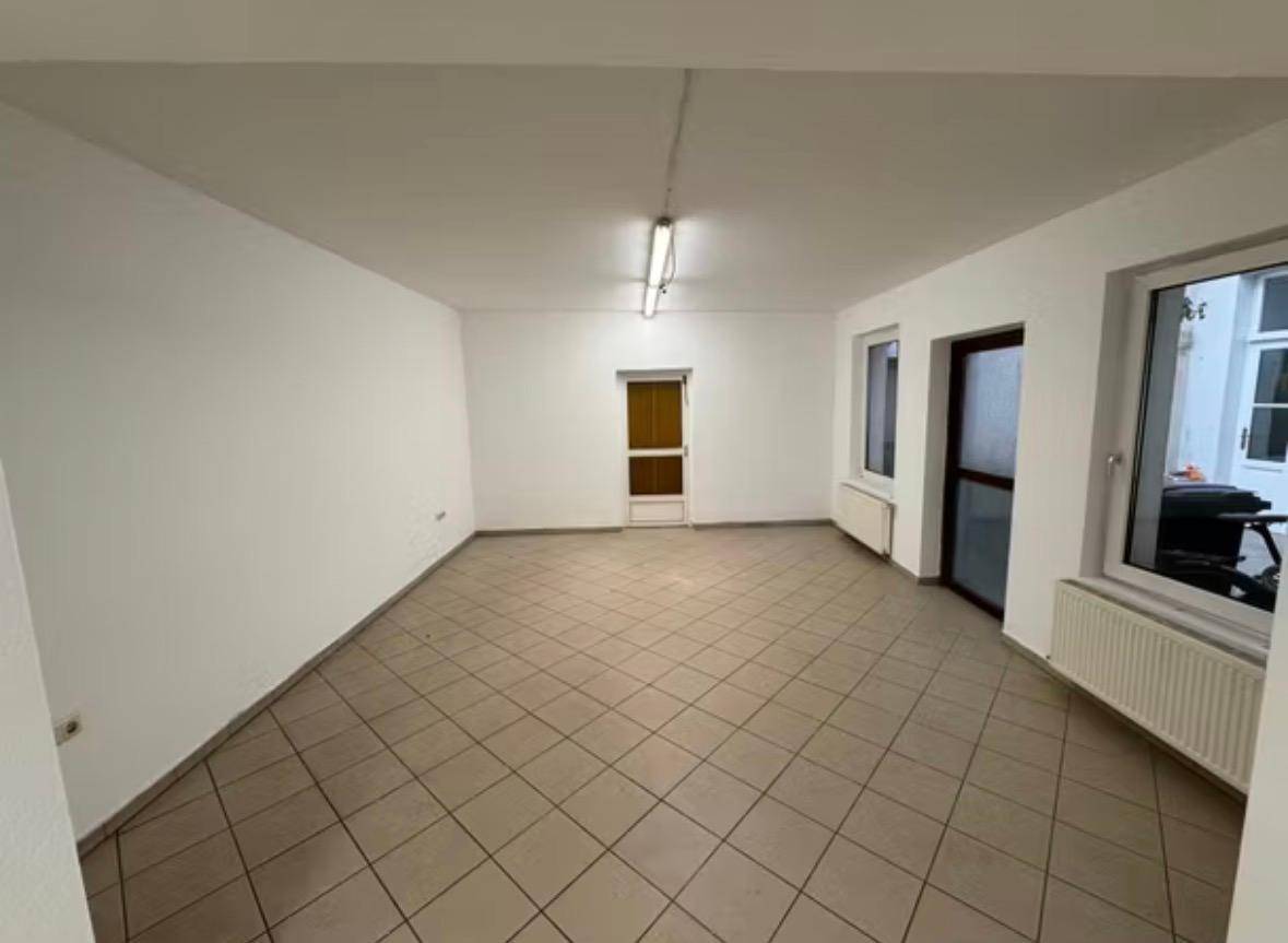 Leerer Gewerberaum mit Fliesenboden, weißen Wänden und Fenstern, die Tageslicht hereinlassen.