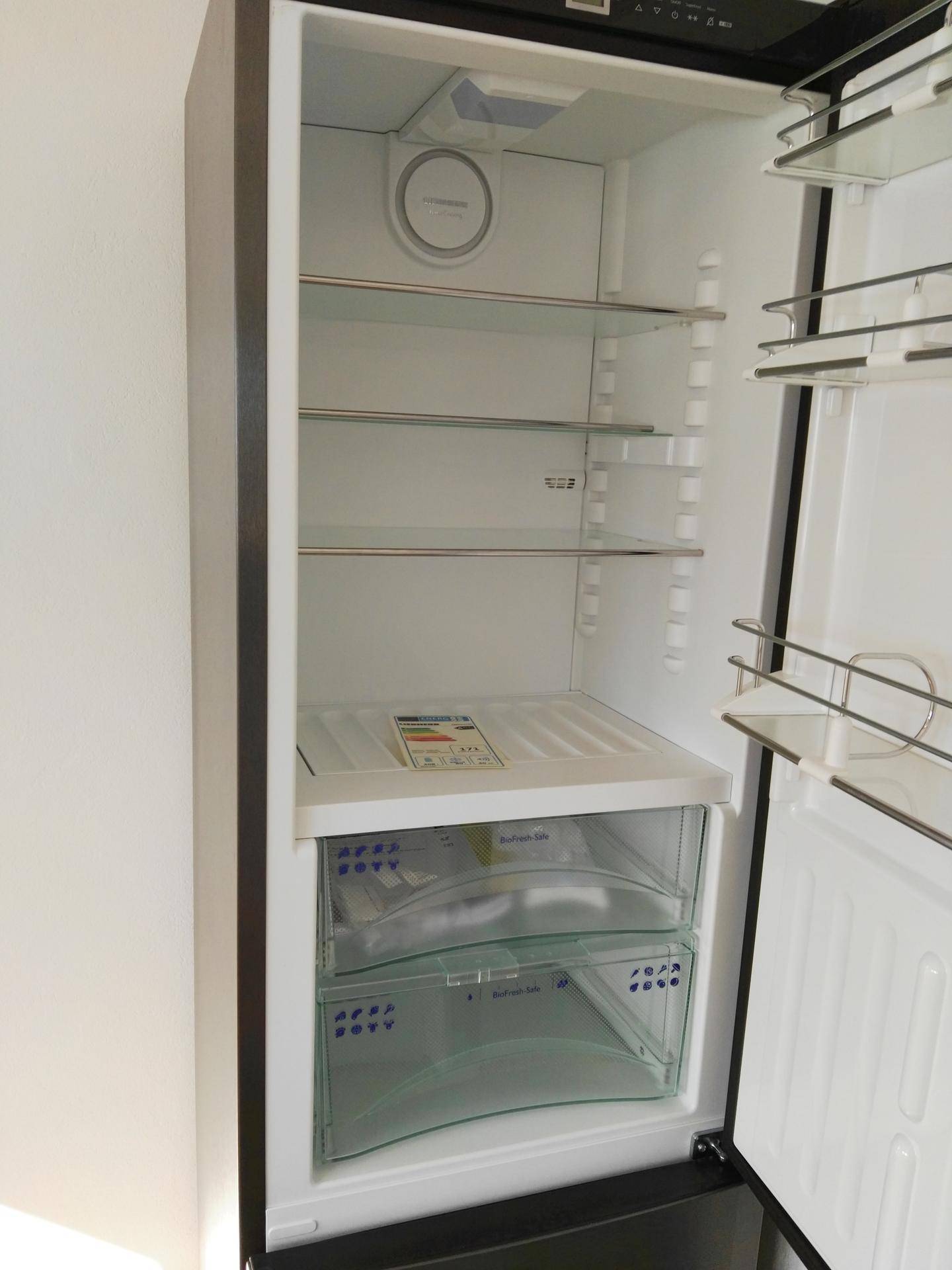 Leerer Kühlschrank mit mehreren Glasablagen und transparenten Gemüsefächern.