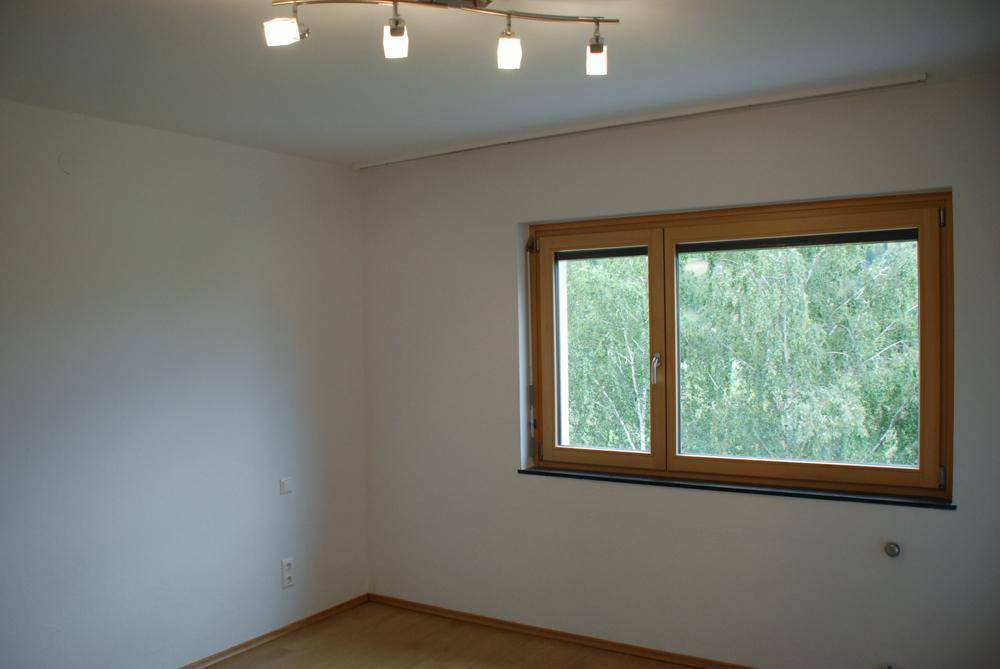 Schlafzimmer mit hellem Holzfußboden und einem Fenster, das einen grünen Ausblick bietet.