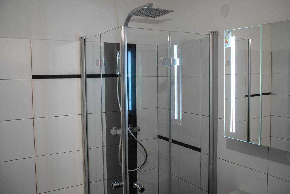 Moderne Duschkabine mit Regendusche und weißen Fliesen, ausgestattet mit einem Spiegelschrank.