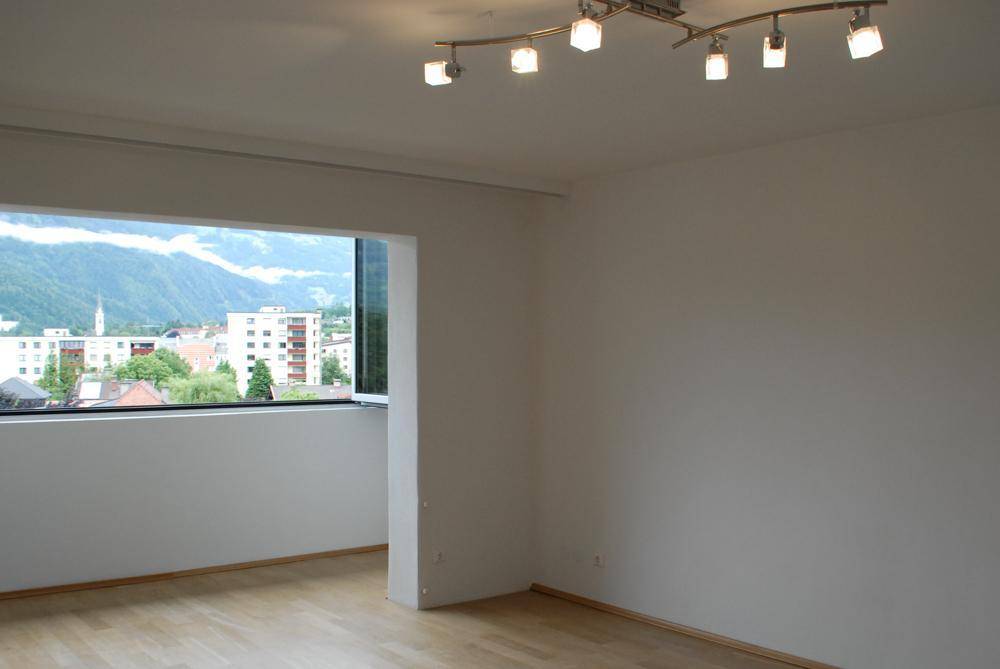 Heller Wohnraum mit Holzfußboden und weitem Blick auf die Stadt und die umliegenden Berge.