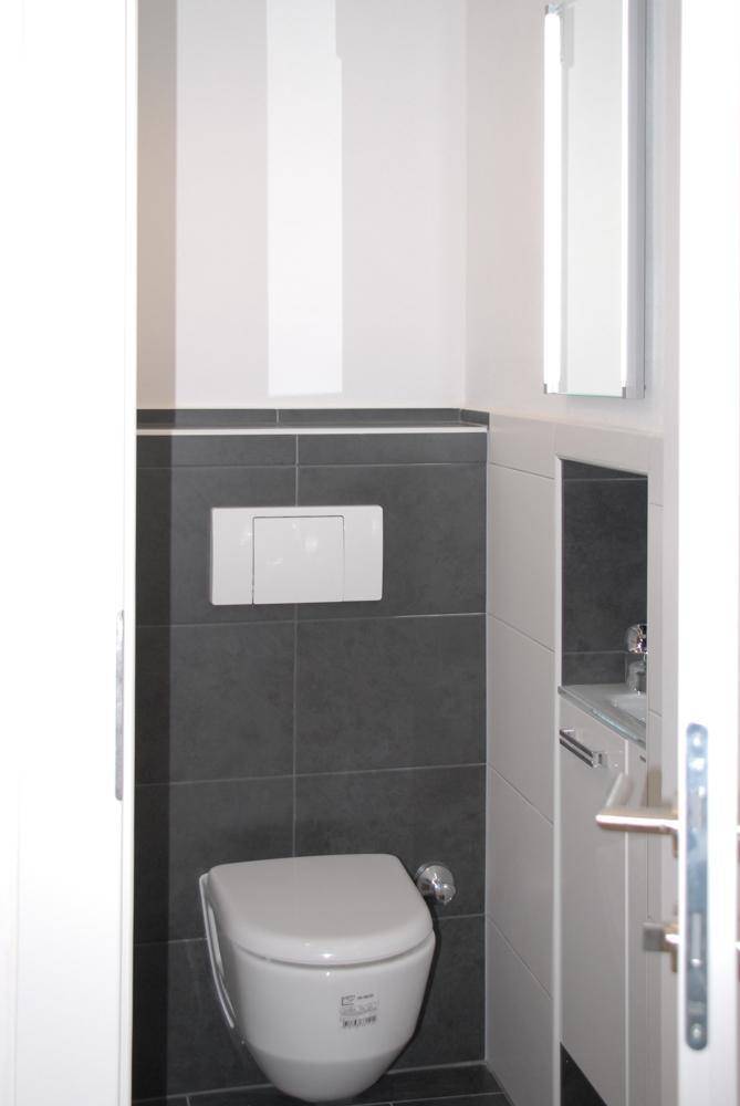 Modernes Gäste-WC mit wandhängender Toilette und stilvollen dunkelgrauen Fliesen.