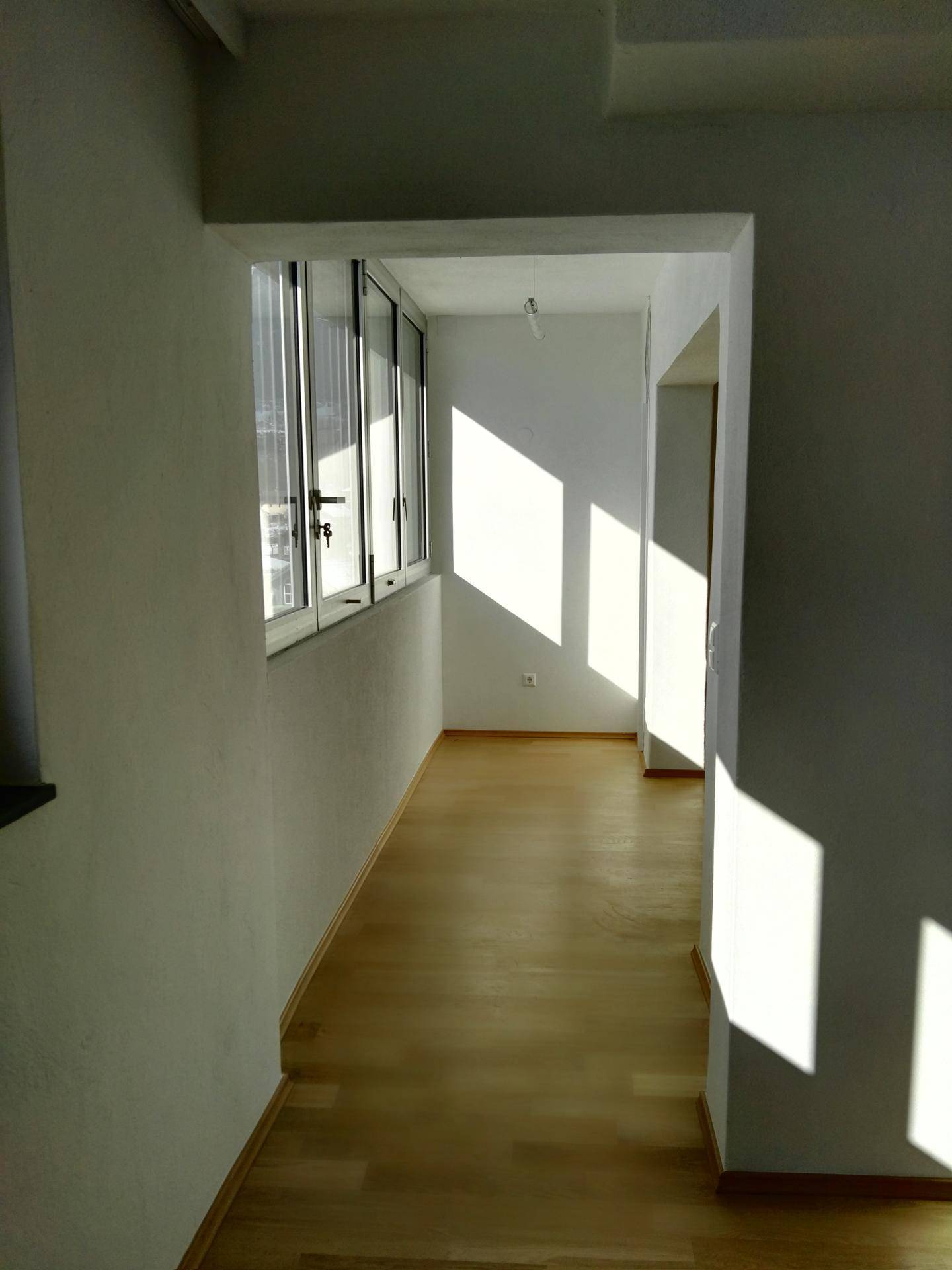 Heller Flur mit Holzfußboden und großen Fenstern, die viel natürliches Licht hereinlassen.