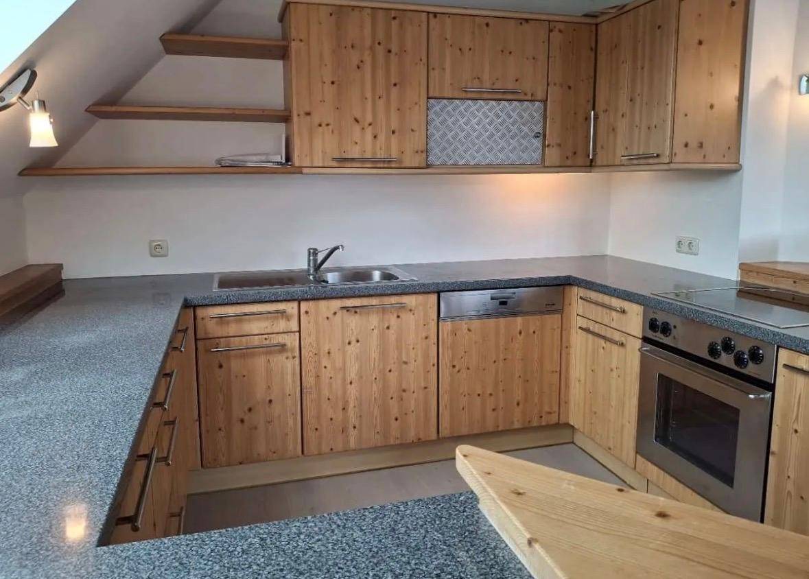 Funktionale Küche mit Holzschränken, grauen Arbeitsplatten und integrierten Geräten.