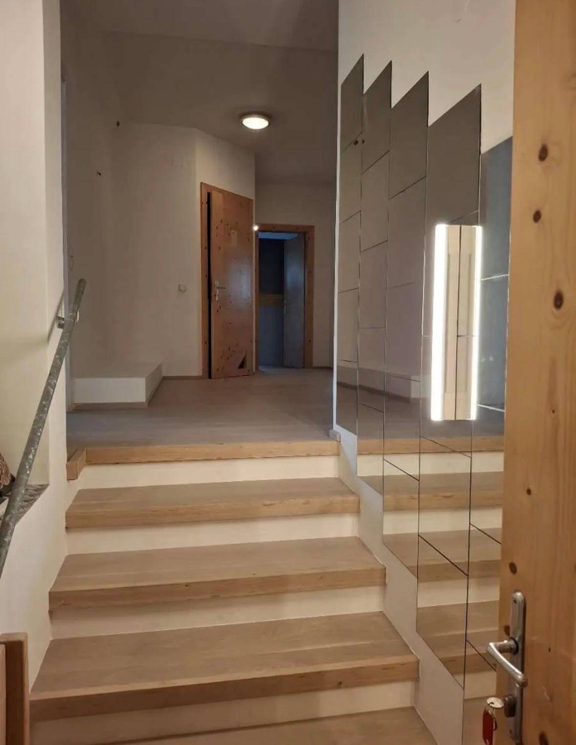Eingangsbereich mit Holztreppe und einer dekorativen Spiegelwand, die den Raum erweitert.