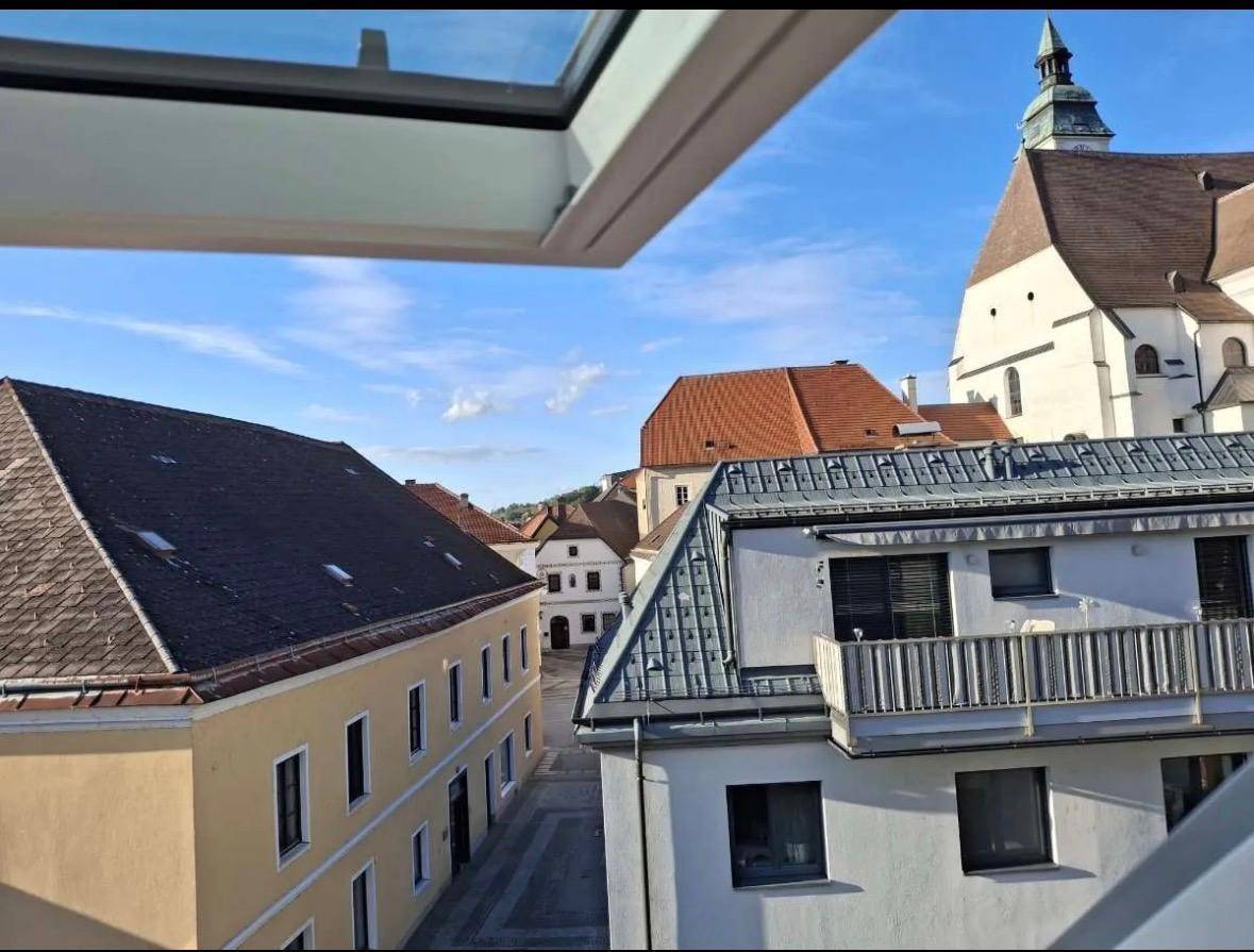 Ausblick aus einem Fenster auf historische Dächer und einen Kirchturm in der Ferne.
