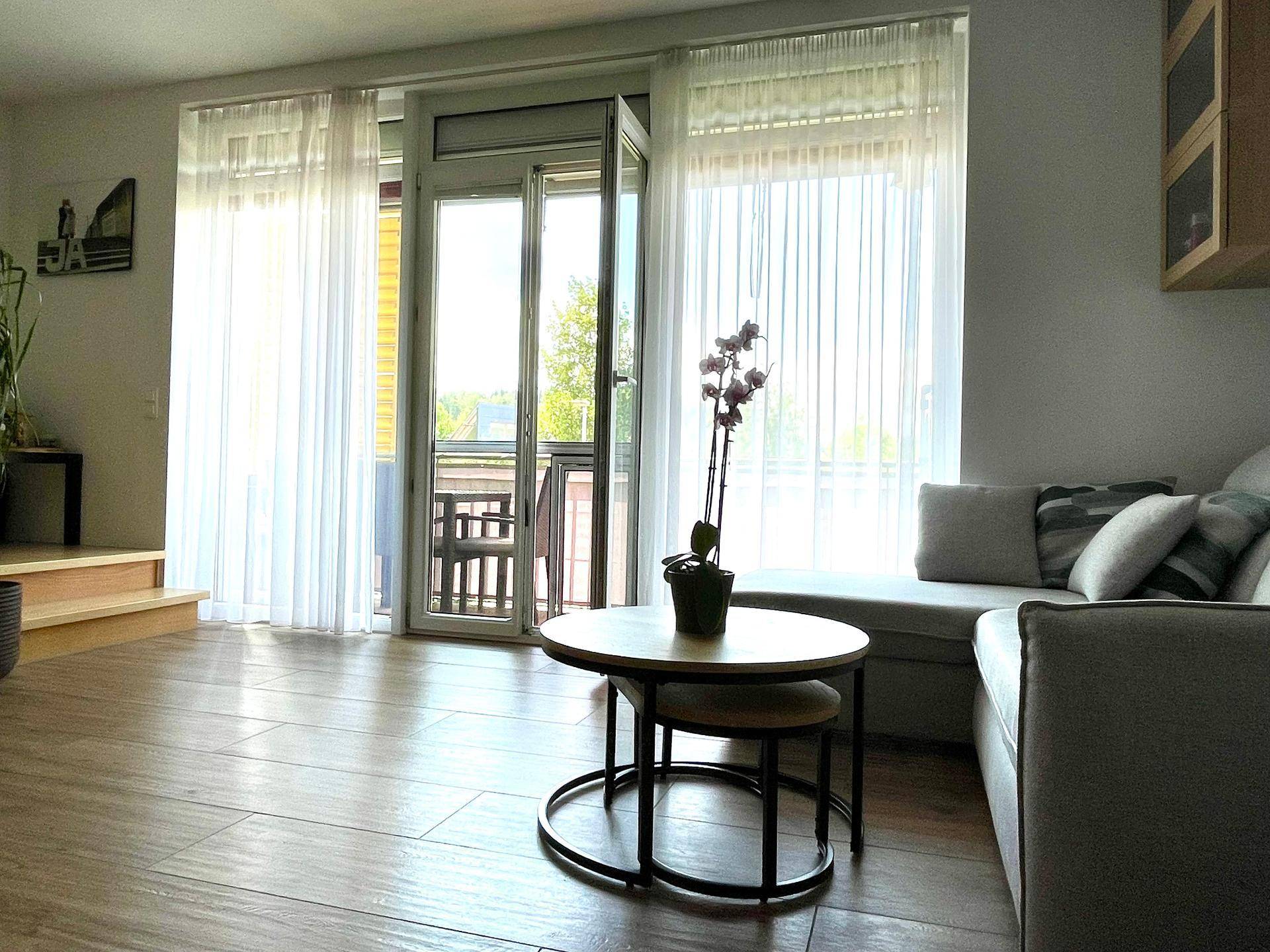 Helles Wohnzimmer mit Holzboden, bequemer Couch und Zugang zu einem Balkon mit viel Tageslicht.