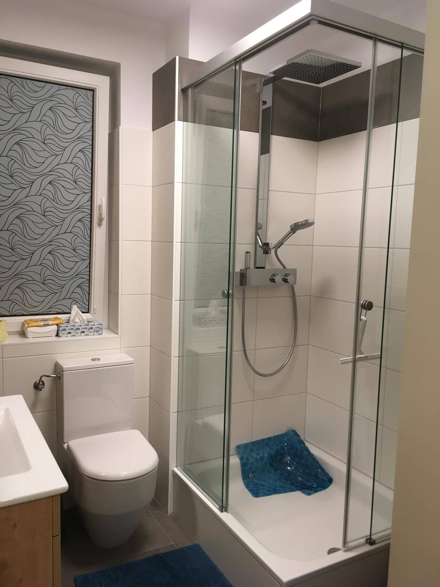Badezimmer mit moderner Duschkabine, Toilette und einem Fenster für natürliche Belüftung und Tageslicht.