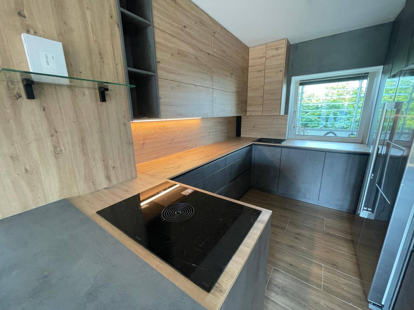 Moderne Küche mit Holz- und grauen Fronten, Induktionskochfeld und integrierter Beleuchtung unter den Oberschränken.