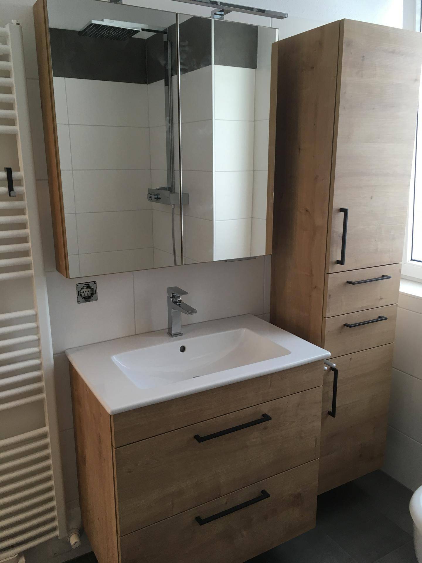 Modernes Badezimmer mit Holzwaschtisch, Spiegelschrank, hohem Stauraumschrank und beheiztem Handtuchhalter.